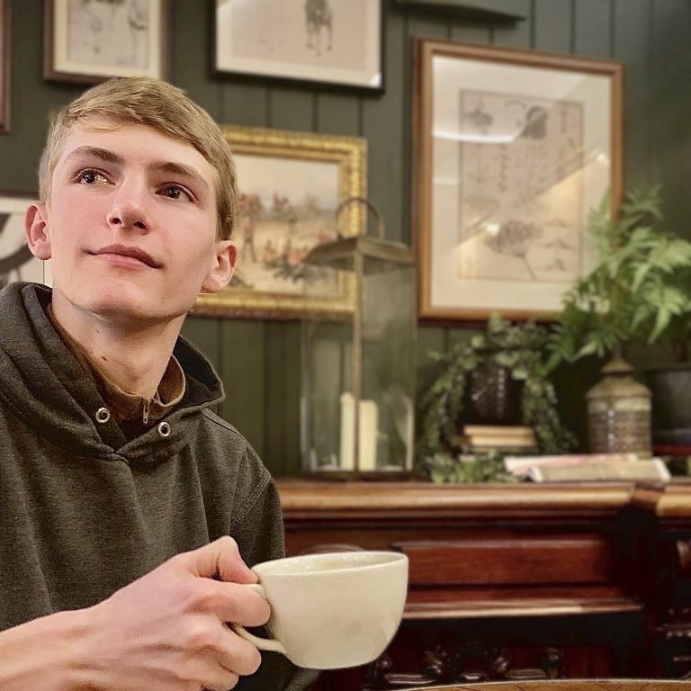 Lucas holding a tea cup and gazing into the distance.